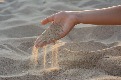 Photo of Girl pouring sand from hand outdoors, closeup. Fleeting time concept