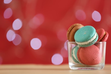 Delicious macarons in bowl on table against blurred background, closeup. Space for text