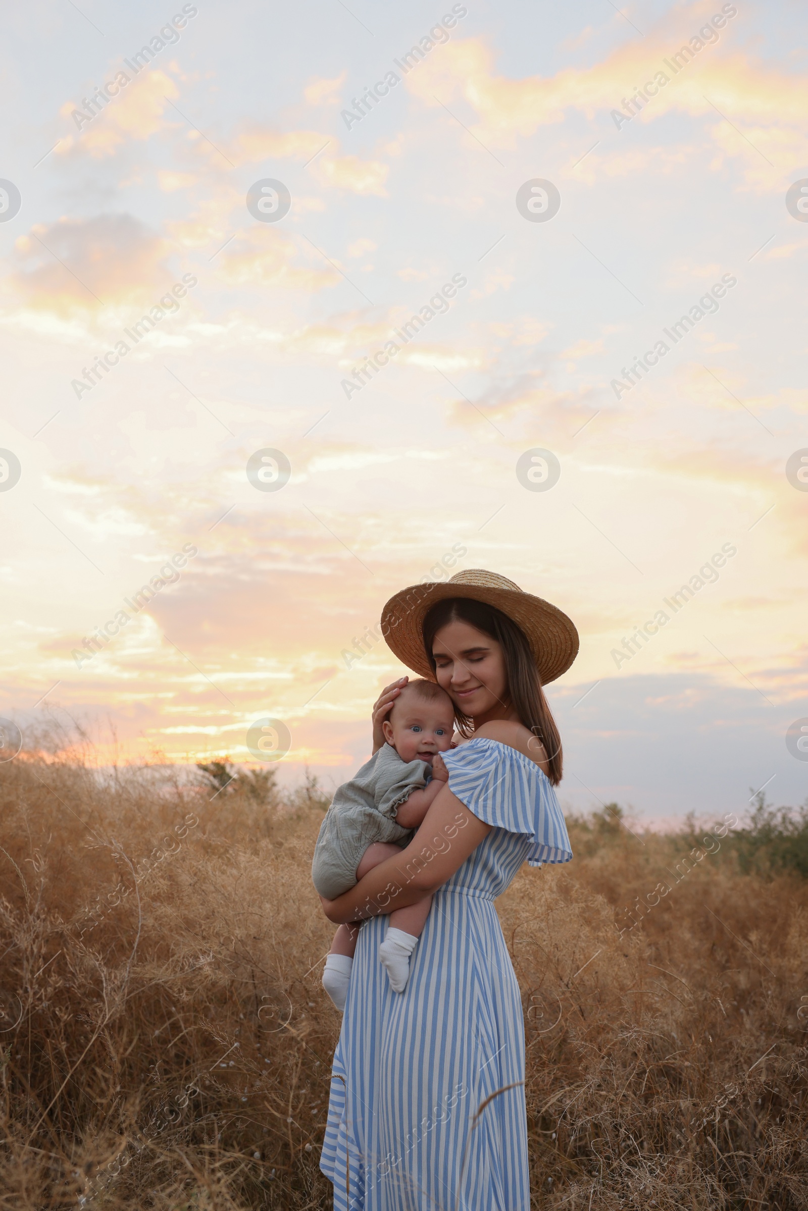 Photo of Happy mother with adorable baby in field at sunset