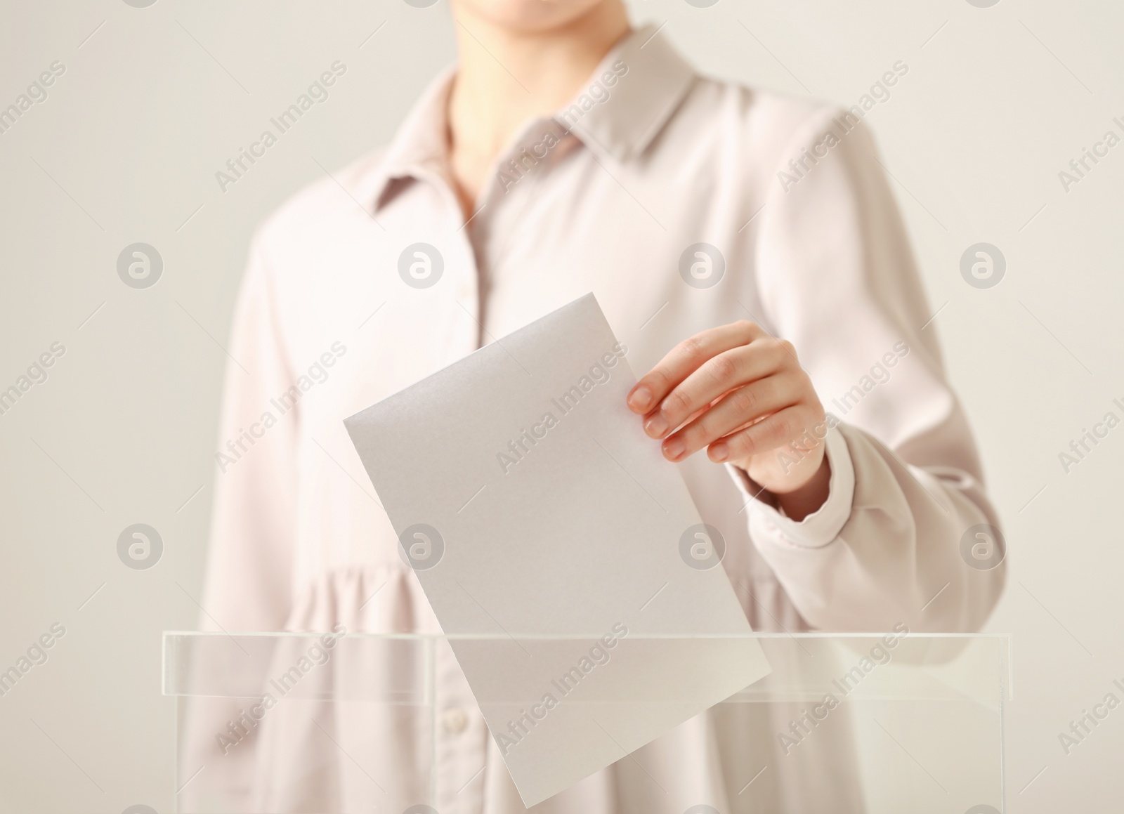 Photo of Woman putting vote into ballot box against light background, closeup