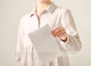 Woman putting vote into ballot box against light background, closeup