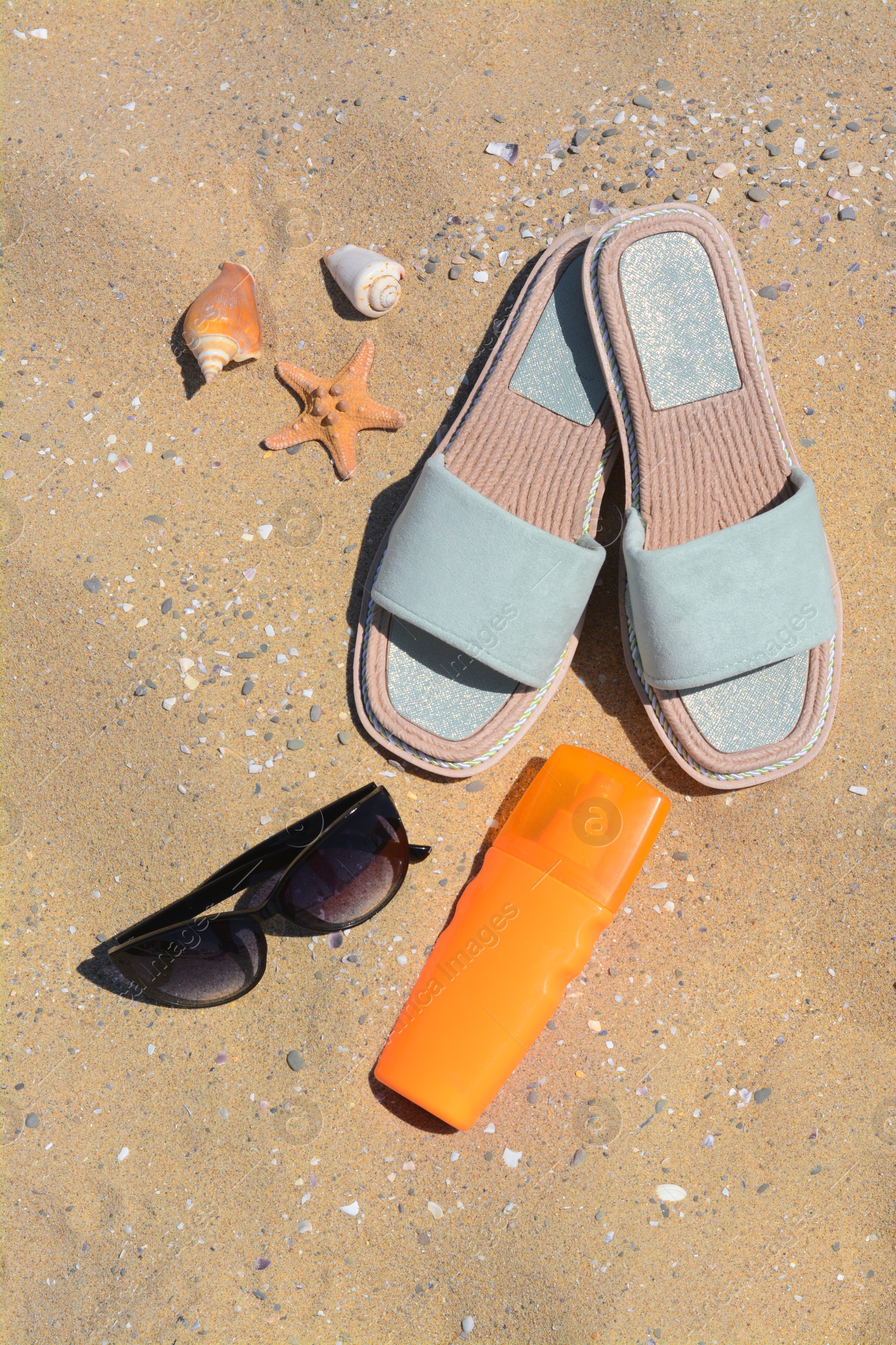 Photo of Stylish sunglasses, slippers and bottle of sunblock on sand. Beach accessories