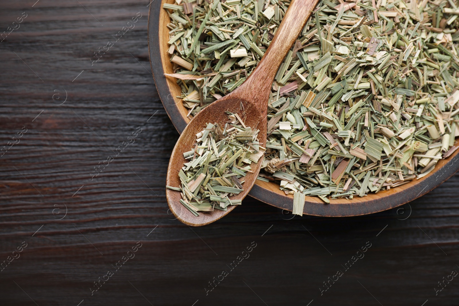 Photo of Bowl with aromatic dried lemongrass and spoon on wooden table, top view