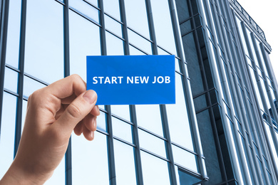 Image of Change your life. Woman holding card with text Start New Job against modern building, closeup