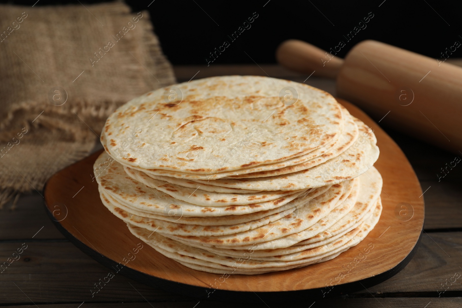 Photo of Many tasty homemade tortillas and rolling pin on wooden table