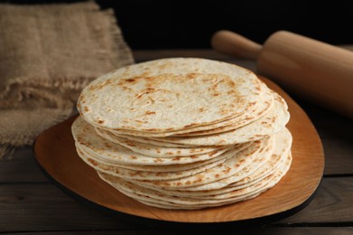 Many tasty homemade tortillas and rolling pin on wooden table