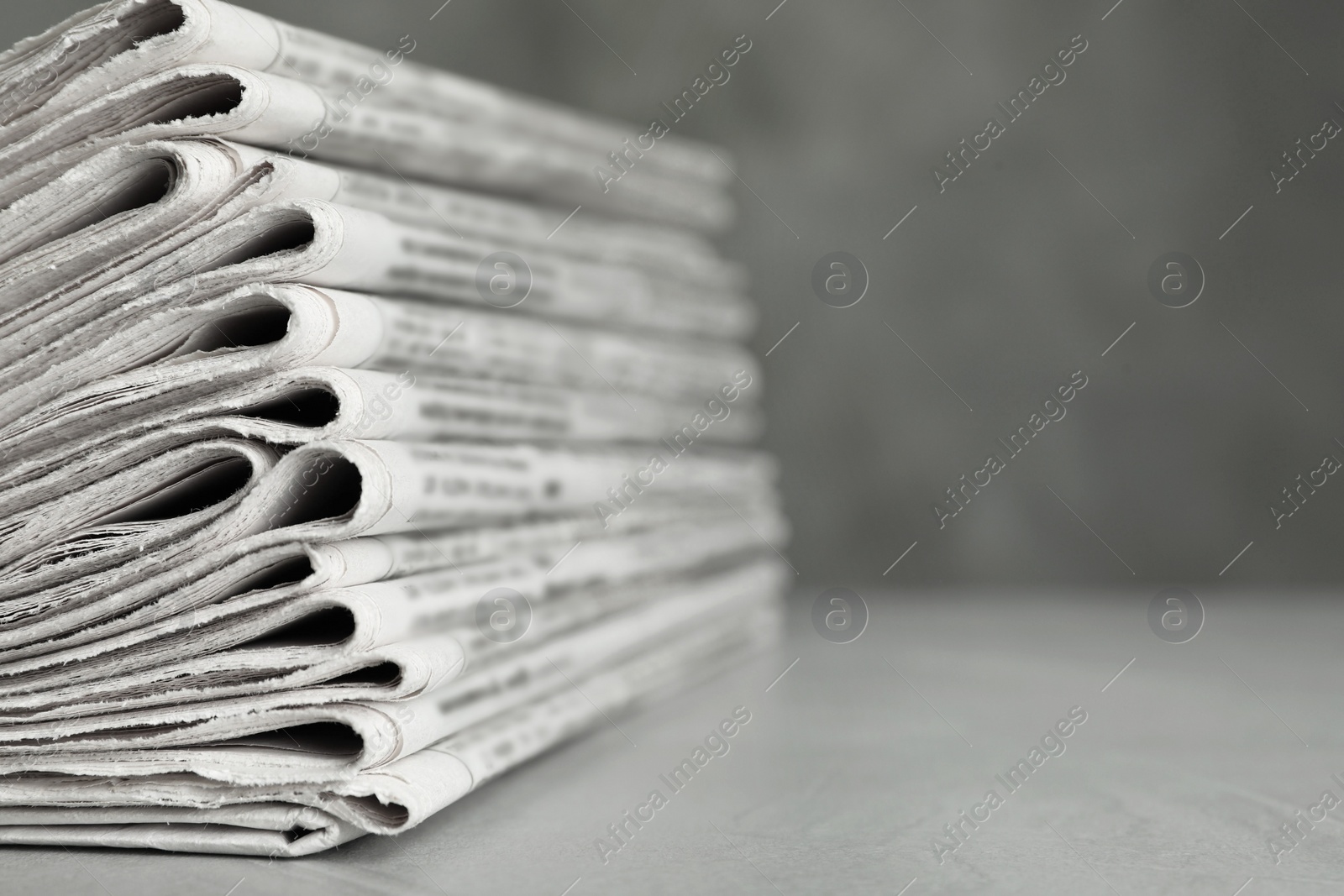 Photo of Stack of newspapers on light grey stone table, closeup with space for text. Journalist's work