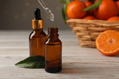 Photo of Tangerine essential oil dripping from pipette into bottle on wooden table