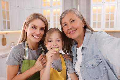 Photo of Three generations. Happy grandmother, her daughter and granddaughter taking selfie in kitchen