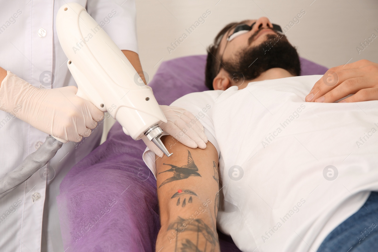 Photo of Young man undergoing laser tattoo removal procedure in salon