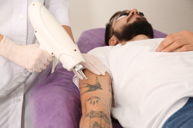 Photo of Young man undergoing laser tattoo removal procedure in salon