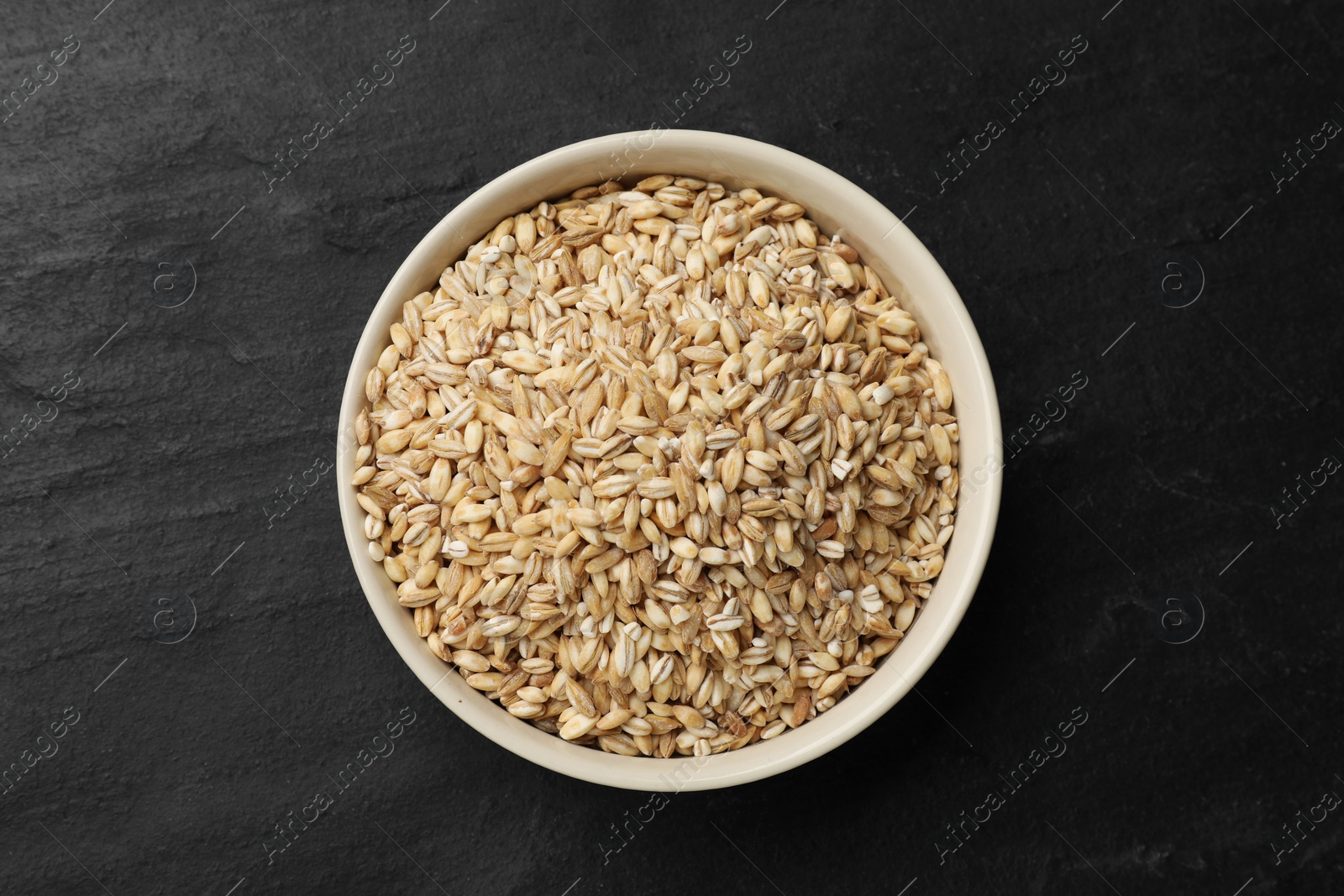 Photo of Dry pearl barley in bowl on dark gray table, top view