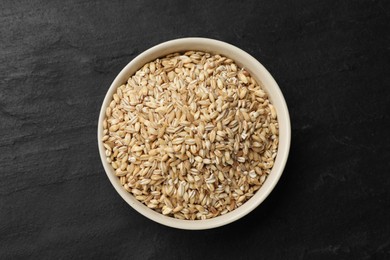 Photo of Dry pearl barley in bowl on dark gray table, top view