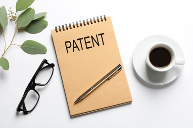Image of Notebook with word PATENT, pen, cup of coffee, glasses and plant on white table, flat lay