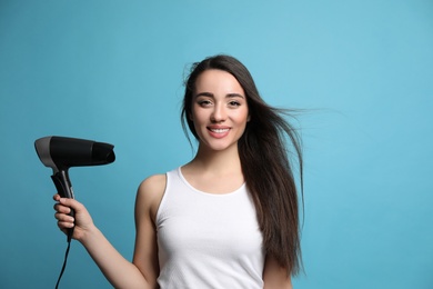 Beautiful young woman using hair dryer on light blue background