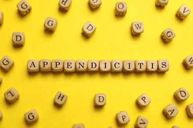 Photo of Word Appendicitis made of wooden cubes with letters on yellow background, flat lay