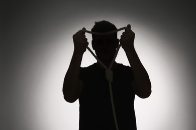 Photo of Silhouette of man with rope noose on light background