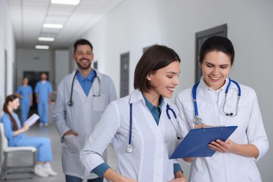 Photo of Smart medical students with clipboard in college hallway, space for text