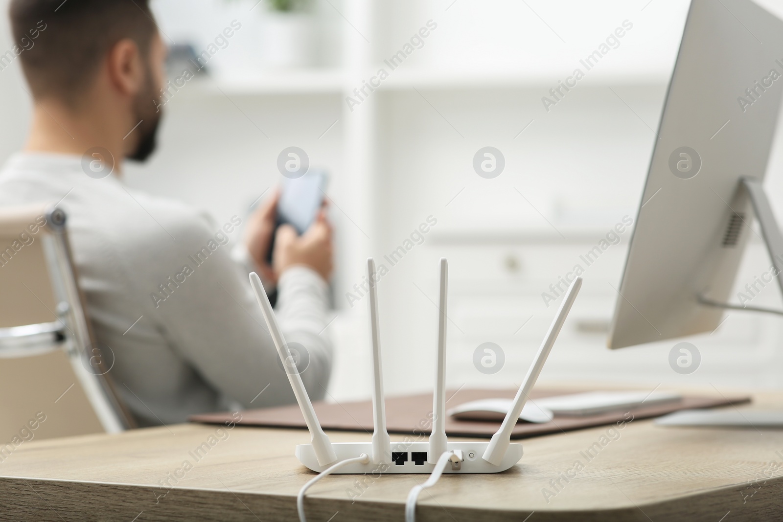 Photo of Man with smartphone working at wooden table indoors, focus on Wi-Fi router