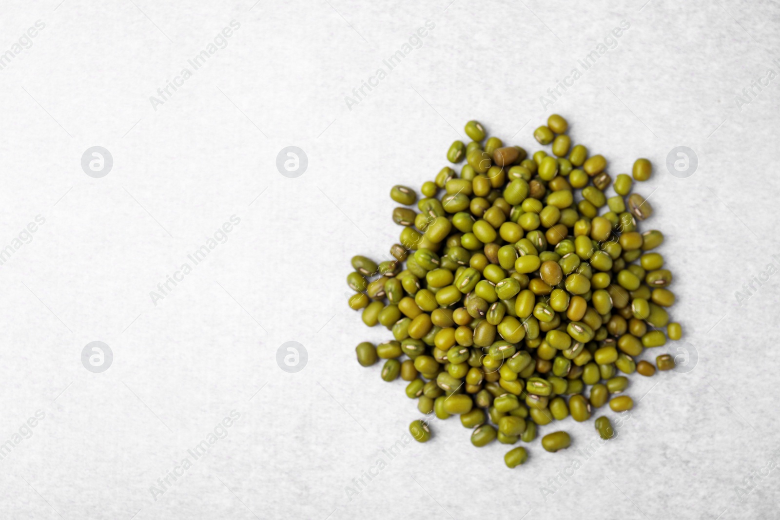 Photo of Pile of green mung beans on light grey table, top view. Space for text