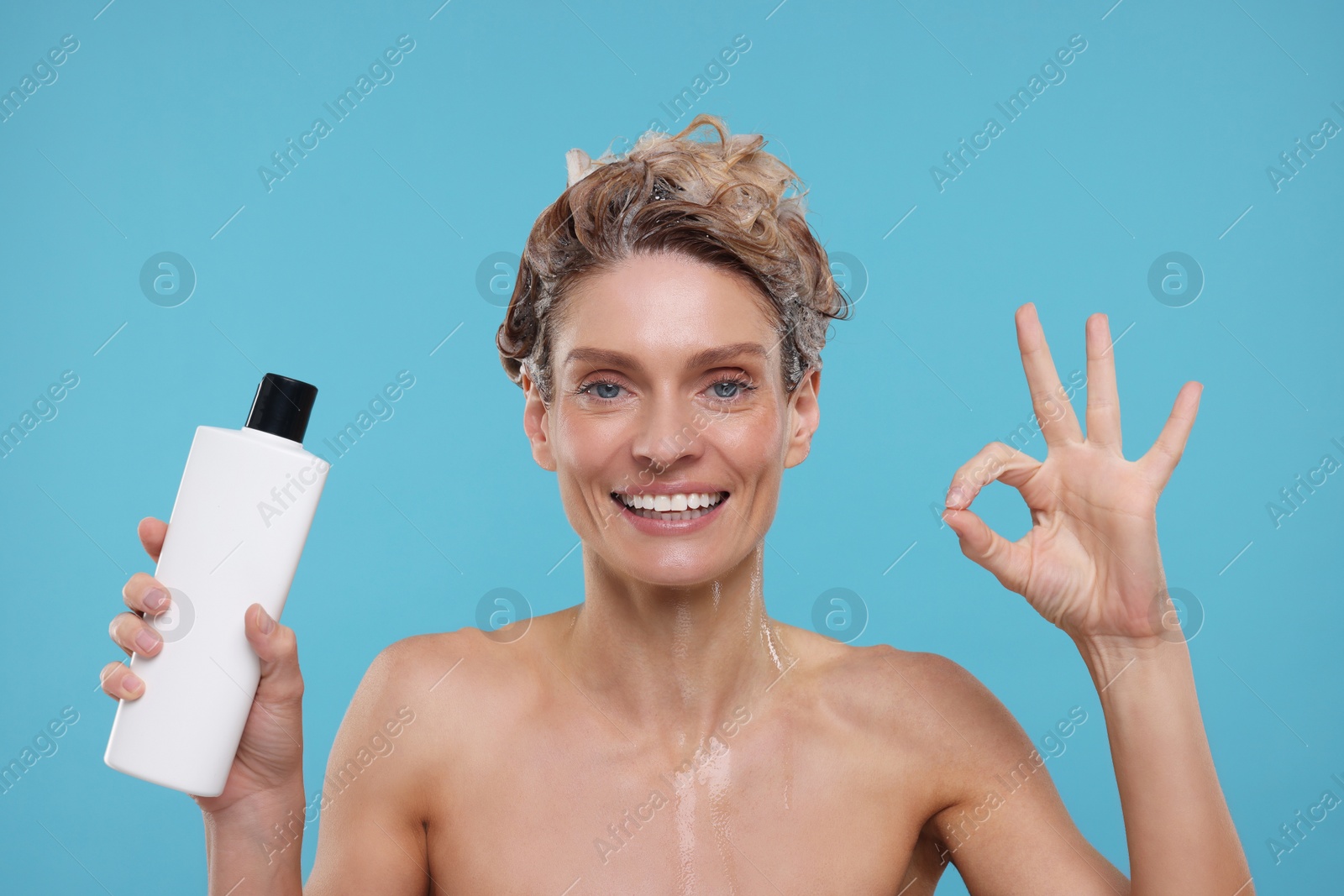 Photo of Washing hair. Portrait of happy woman with bottle showing ok gesture on light blue background