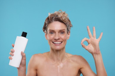 Photo of Washing hair. Portrait of happy woman with bottle showing ok gesture on light blue background