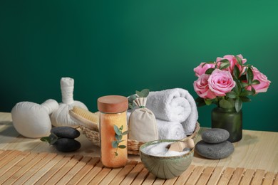 Photo of Beautiful composition with sea salt, flowers and different spa products on wooden table near green wall, space for text