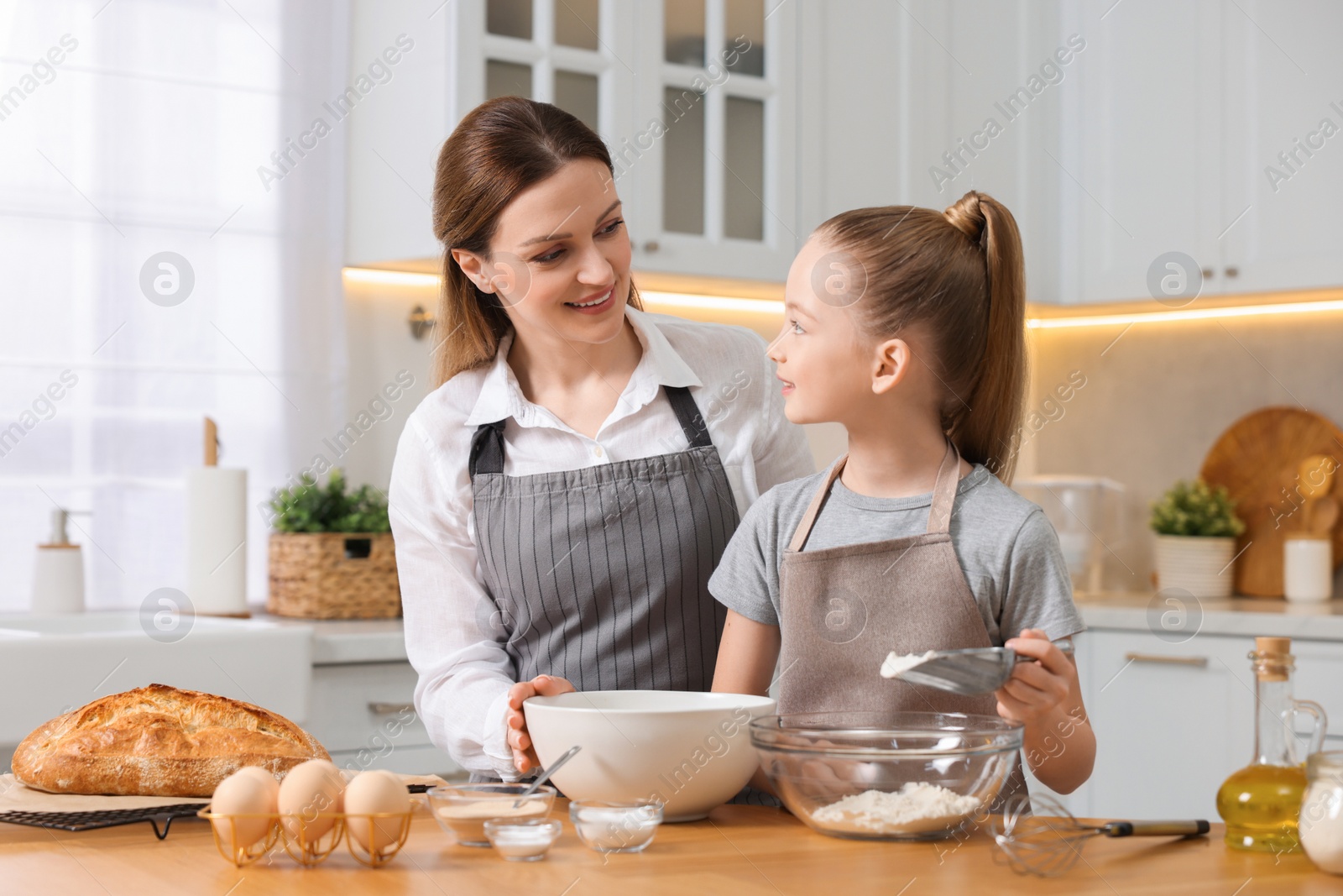 Photo of Making bread. Mother and her daughter preparing dough at wooden table in kitchen