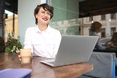 Photo of Young woman working with laptop at desk in cafe