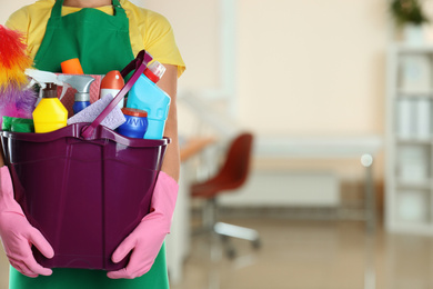 Image of Woman holding bucket with cleaning supplies in office, closeup. Space for text