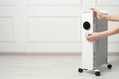 Photo of Young woman adjusting temperature on modern electric heater indoors, closeup. Space for text