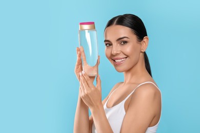 Photo of Young woman with bottle of micellar water on light blue background