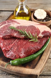 Fresh raw beef cut with spices and oil on wooden table, closeup