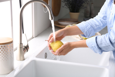 Photo of Woman washing fresh ripe pear in kitchen, closeup
