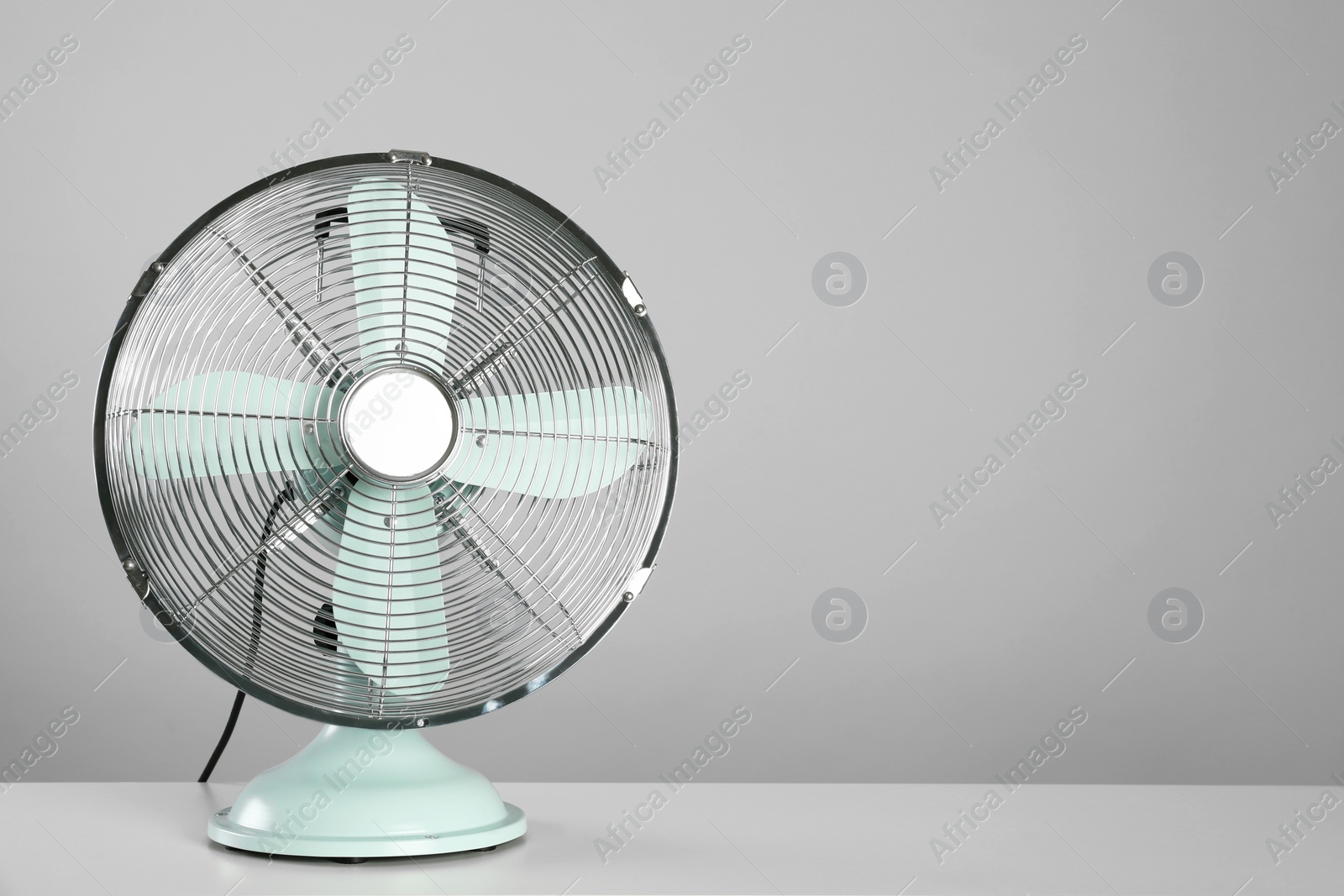 Photo of Electric fan on table against light grey background, space for text. Summer heat