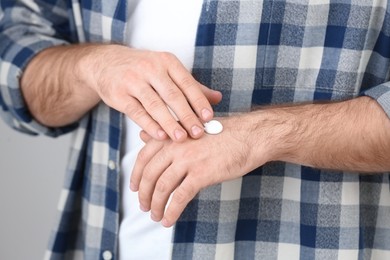 Man applying cream onto hand on light grey background, closeup