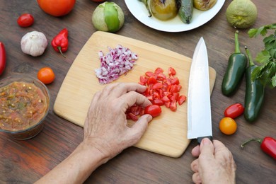 Photo of Woman cutting tomato for salsa sauce at wooden table, view from above