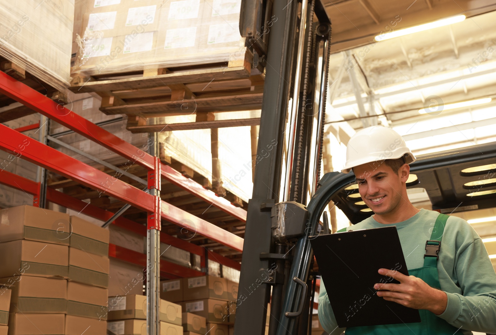 Image of Worker near forklift truck with cardboard boxes in warehouse. Logistics concept