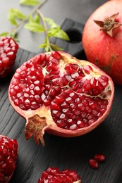 Photo of Cut fresh pomegranate and green leaves on table, closeup