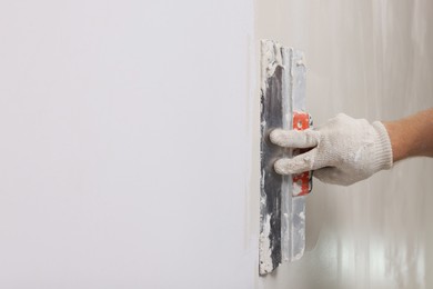 Photo of Worker plastering wall with putty knife indoors, closeup. Space for text