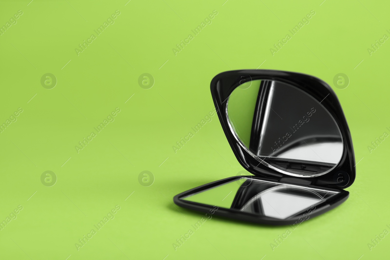 Photo of Stylish cosmetic pocket mirror on light green background. Space for text