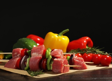 Photo of Skewers with fresh raw meat and vegetables on table against dark background