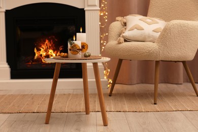 Photo of Beautiful burning candles decorated with dry orange slices and cinnamon sticks on white table in room. Christmas atmosphere