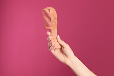 Photo of Woman holding wooden hair comb against crimson background, closeup. Space for text