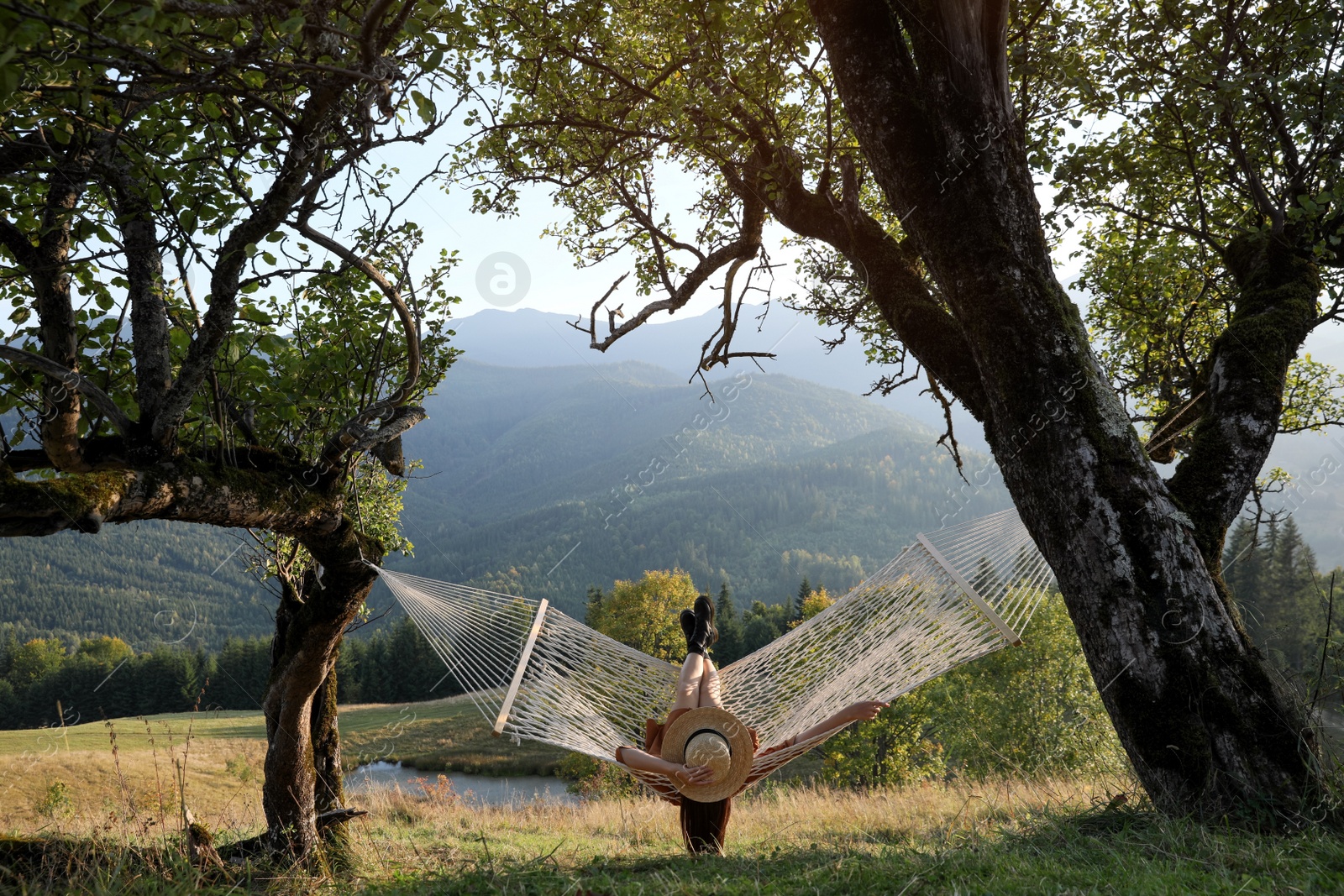 Photo of Young woman resting in hammock outdoors at sunset