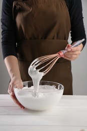 Photo of Woman making whipped cream with whisk at white wooden table, closeup