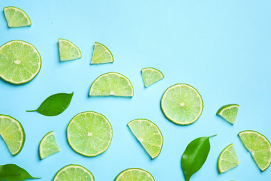 Photo of Juicy fresh lime slices and green leaves on light blue background, flat lay. Space for text