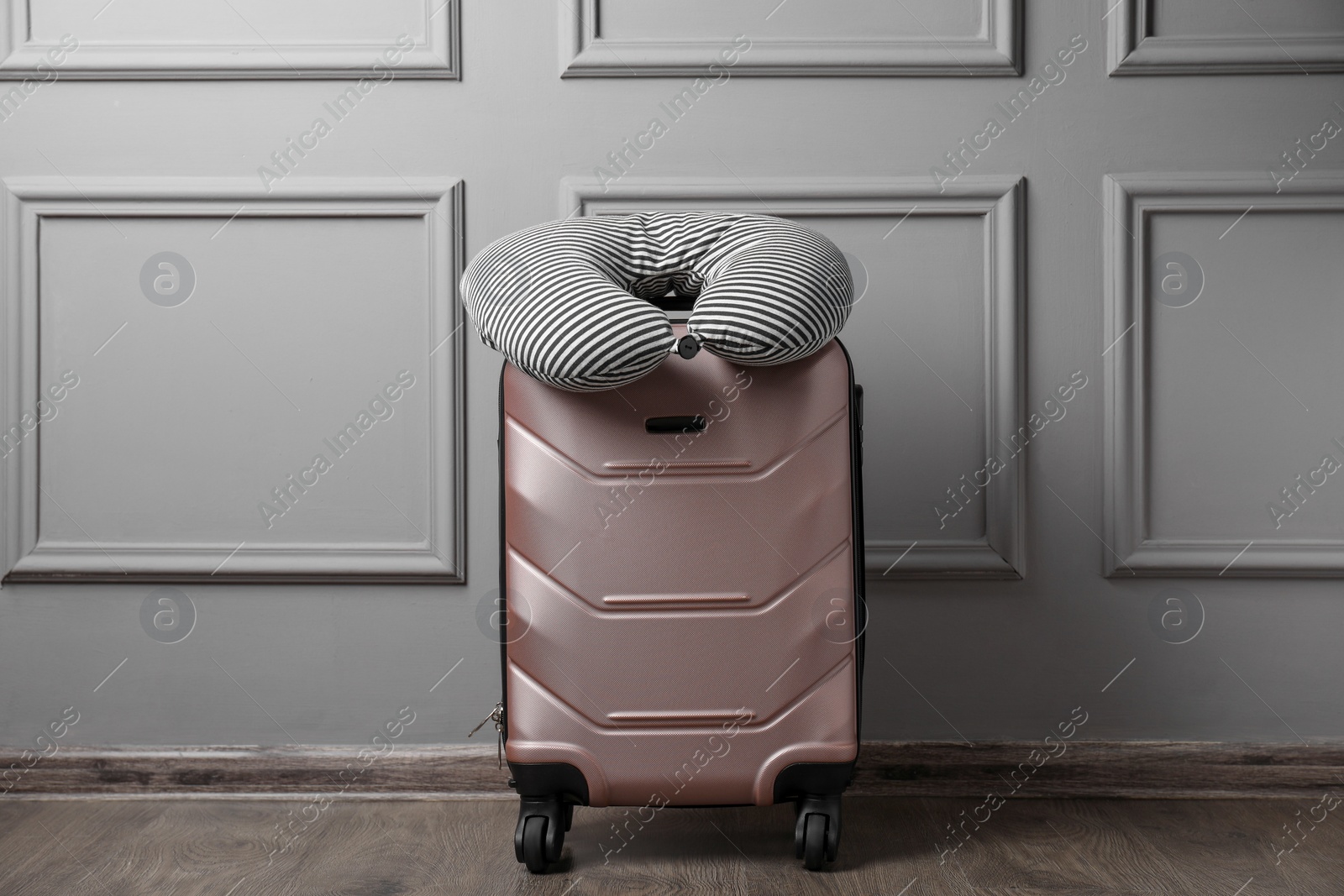 Photo of Striped travel pillow on suitcase near light wall indoors