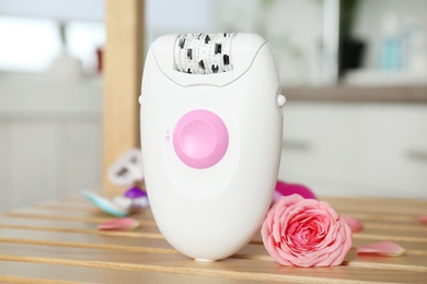 Photo of Modern epilator and beautiful flower on table