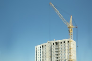 Photo of Blurred view of unfinished building and tower crane against blue sky, space for text